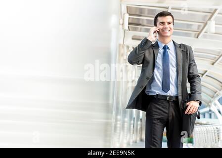 Young handsome hispanic businessman walking and calling on mobile phone at covered walkway in the city Stock Photo