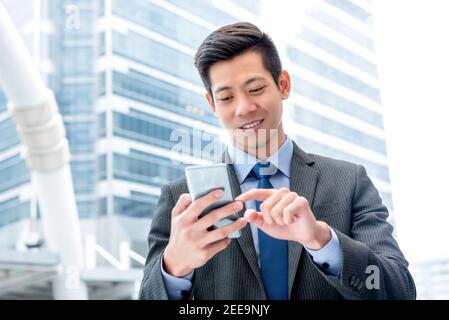 Young handsome Asian businessman  using mobile phone surfing internet searching for online information Stock Photo