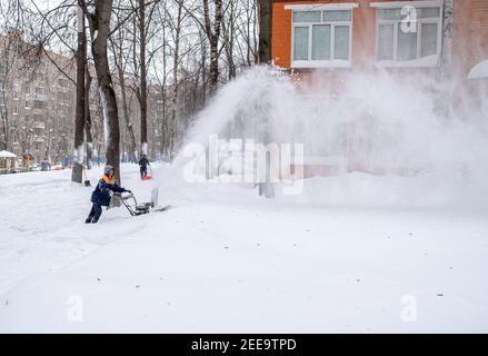 Moscow. Russia. February 13, 2021. A utility worker cleans a path with a snow blower during heavy snow on a winter day. A jet of snow takes off into Stock Photo
