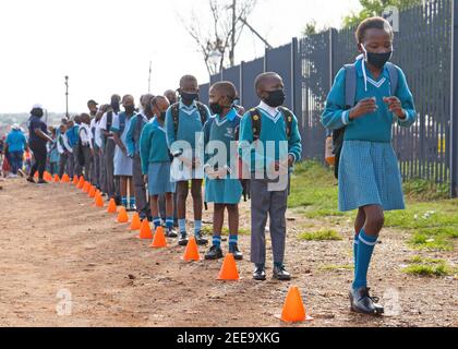 Johannesburg, South Africa. 15th Feb, 2021. Pupils wait in line to get their body temperature checked at the gate of a primary school in Johannesburg, South Africa, Feb. 15, 2021. Over 20,000 public schools in South Africa were reopened in accordance with strict adherence to the COVID-19 protocol on Monday. Credit: Matthew Martin Brink/Xinhua/Alamy Live News Stock Photo