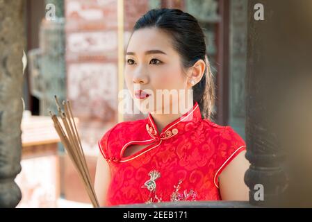 Asian woman in traditional red qipao dress praying with incense sticks during Chinese or Lunar new year Stock Photo