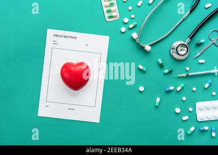 Drugs and medical instruments including stethoscope, syringe, scissors and prescription with red heart shape ball on green background Stock Photo