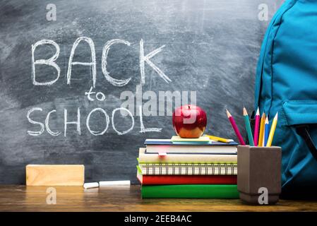 Colorful books and education supplies on wooden table in classroom with back to school handwritten text on blackboard Stock Photo