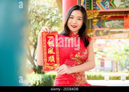 Smiling Asian woman in traditional red cheongsam qipao dress showing Chinese New Year greeting text sign said 'everything will be good' Stock Photo