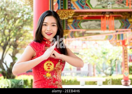 Smiling Asian woman in traditional red cheongsam qipao dress making salute with Chinese new year greeting sign in hand said 'happiness and good fortun Stock Photo