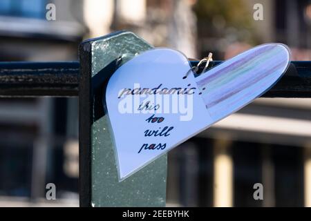 Plasticized paper heart with handwritten text 'Pandamic: this too will pass' hangs from the railing of a bridge in Lemmer, the Netherlands Stock Photo
