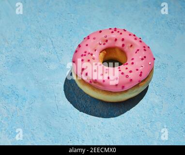Donut with pink frosting and sprinkles on blue background. Stock Photo