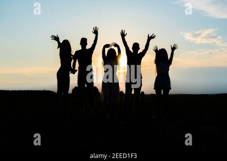 Cohesion concept. Black silhouettes of friends holding hands stands at sunset. Stock Photo