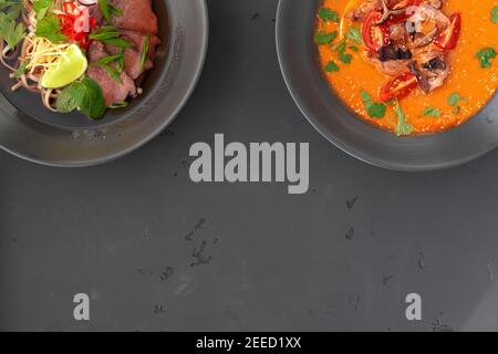 Tom Yam soup and Ramen soup in bowls on gray background Stock Photo