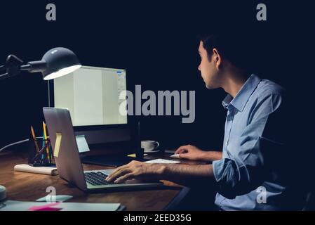Young businessman staying overtime late at night in the office focusing on working with computer at his desk Stock Photo