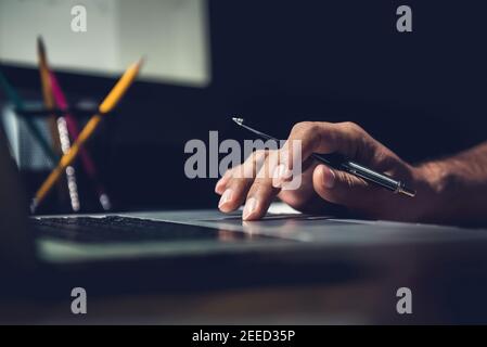 Hand of a man using laptop computer working overtime at his desk in the office late at night Stock Photo