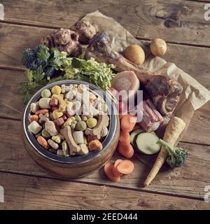 Bowl of premium dried dog biscuits with assorted fresh vegetable ingredients and bones for a balanced diet with vitamins, calcium and protein in squar Stock Photo
