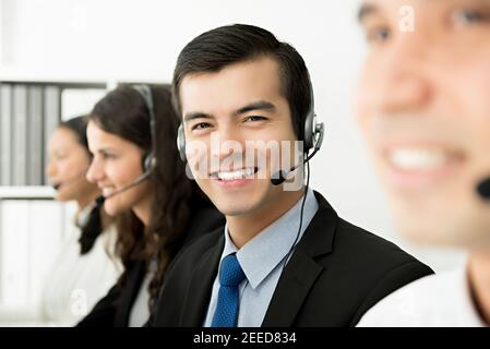 Friendly handsome hispanic man telemarketing customer service agent working in call center office with his team Stock Photo