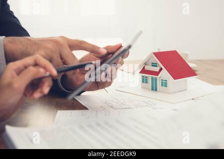 Real estate agent with client or architect team checking a housing model and its blueprints digitally using a tablet Stock Photo