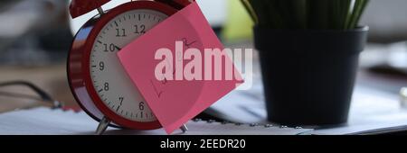 Red alarm clock standing on table near flowerpot in office closeup Stock Photo