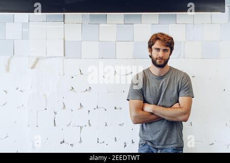 Portrait of a young bearded man standing against grunge weathered wall Stock Photo