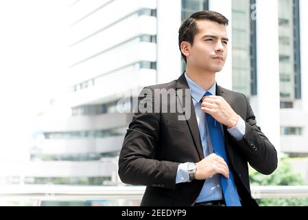 Young handsome hispanic businessman adjusting his necktie while waiting to meet someone outdoors in the city Stock Photo