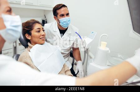 Woman sitting in dentist's chair looking at her dental x-ray with doctors around. Dentist showing x-ray to patient and explaining the procedure of tre Stock Photo