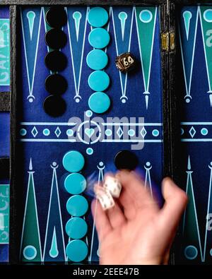A game of backgammon on a colorful board, with one hand rolling the dice Stock Photo