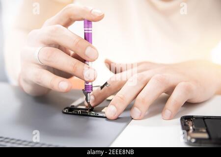Master disassembles modern mobile phone, repairs and replaces battery, broken screen. Stock Photo