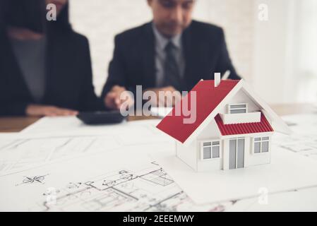 Real estate agent discussing work with blueprints and house model on the table - property appraisal and valuation concept Stock Photo