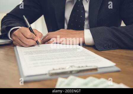 Businessman signing legal business contract agreement with money on the table Stock Photo