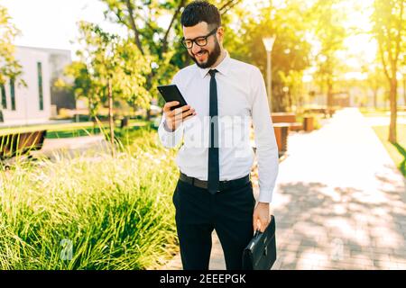 Happy elegant businessman with glasses uses mobile phone while walking in the city Stock Photo
