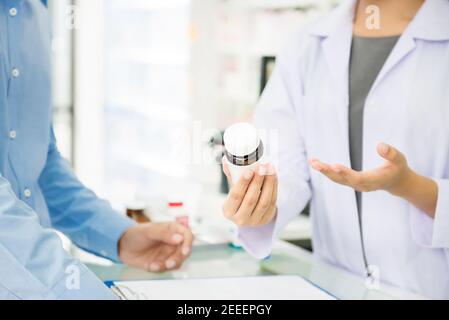 Female pharmacist holding medicine bottle giving advice to customer in chemist shop or pharmacy Stock Photo