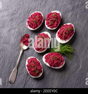 Stuffed eggs with beetroot with cream cheese, garlic and spicy herbs on a black slate background, top view. delicious homemade food Stock Photo