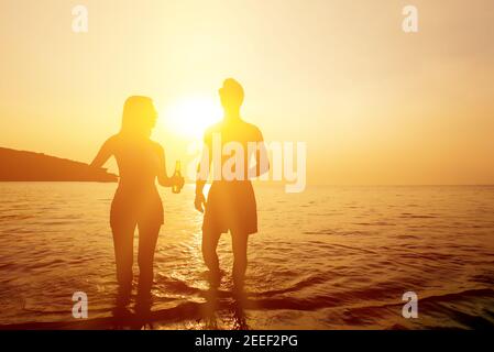 Silhouette of couple walking in seawater at the beach in twilight ...