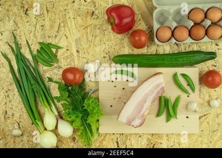 Fresh chicken eggs and bacon with vegetables. Background and Space for text. Vegetables for omelet or scrambled eggs are laid out on the table. Vegeta Stock Photo