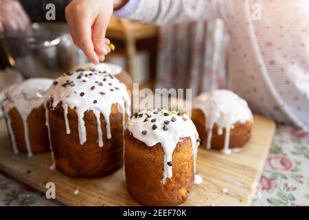 Kid help mom decorate Traditional eastern europe Russian and ukrainian Easter cake kulich decorated with sweet sugar icing on wooden table morning Stock Photo