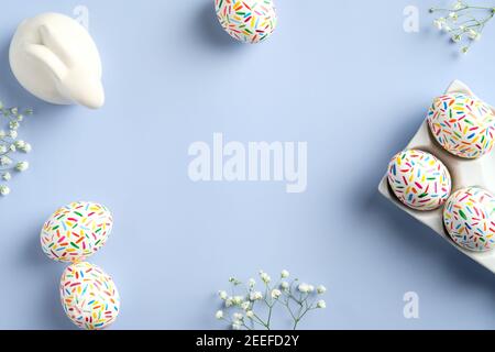 Happy Easter card. Frame made of colorful speckled Easter eggs, spring flowers, Easter bunny. Flat lay, top view, copy space. Stock Photo