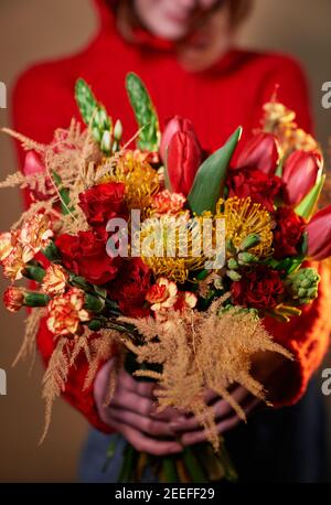 Beautiful girl in red sweater and jeans holding colored bouquet of roses, carnation flowers and other. St. Valentine's Day, International Women's Day Stock Photo
