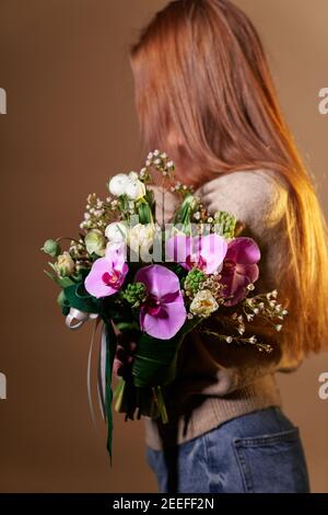 Beautiful woman in beige sweater and jeans with flower bouquet, no face, spring theme. Mother's Day, St. Valentine's day or International Woman's Day Stock Photo