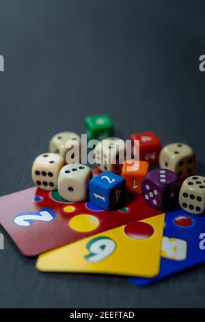 Colourful dice lie on colourful playing cards against a dark, neutral background. Stock Photo