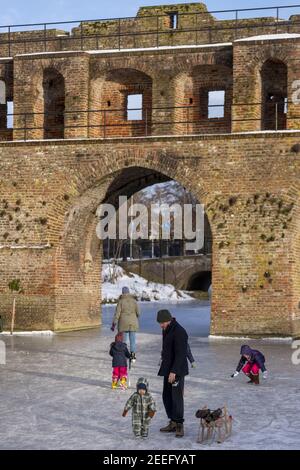 ZUTPHEN, NETHERLANDS - Feb 14, 2021: Family in front of medieval portal construction in historic center with frozen Berkel river Stock Photo