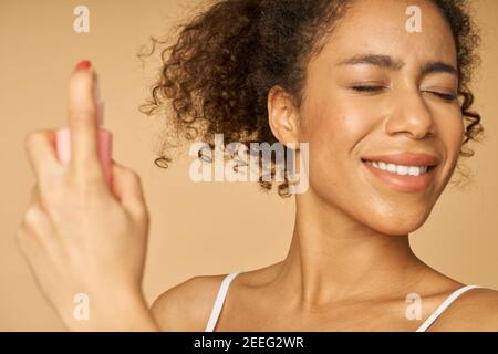 Close up portrait of happy young woman applying spray water on her face, posing isolated over beige background. Beauty, skincare routine concept Stock Photo