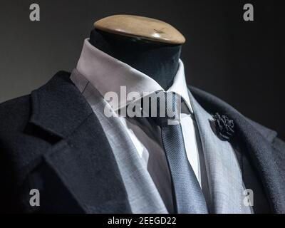 Men formal Suit, with a white shirt, a black tie, and a black lapel flower pin and grey jacket on display on dummy in front of a tailor store, on a wi Stock Photo