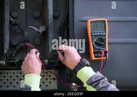 Concept: work and technology. Detail of hands testing a battery with a voltmeter. Stock Photo