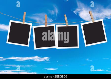 Four blank instant photo frames hanging on a rope, on blue sky background Stock Photo