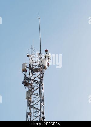 Concept: vertical work. Two technicians working on a tall and dangerous metal tower with antennas. Stock Photo