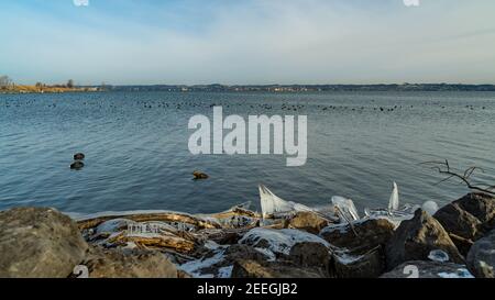 Tench holes in the morning light in winter cold. Shore of Lake Constance with natural ice created sculptures. german shore with Lindau  in Background Stock Photo
