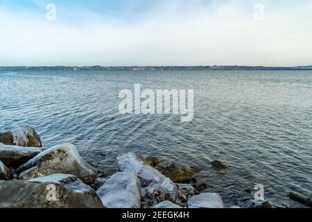 Tench holes in the morning light in winter cold. Shore of Lake Constance with natural ice created sculptures. german shore with Lindau  in Background Stock Photo