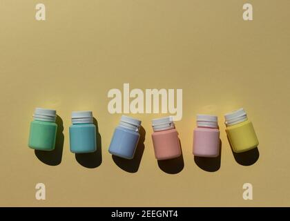 Cans of multi-colored acrylic paints in pastel colors in a row on a yellow background. A minimalistic composition with hard shadows. Copy space Stock Photo