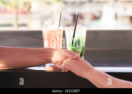 Male and female hands with cocktails. Closeup of couple hands, two cocktails. Romantic couple at drinking in a restaurant. Love, Marriage proposal and Stock Photo