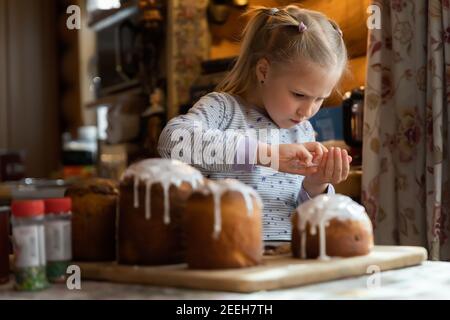 Kid help mom decorate Traditional eastern europe Russian and ukrainian Easter cake kulich decorated with sweet sugar icing on wooden table morning Stock Photo
