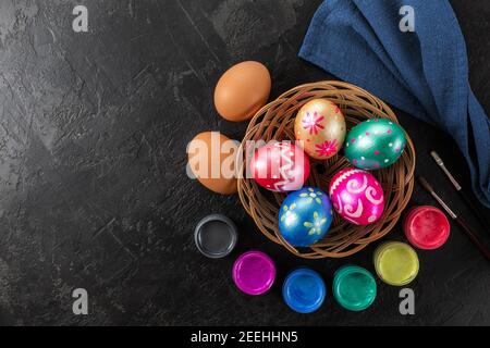Multicolored easter painted handmade eggs, paints and brushes. Festive Easter frame from eggs, paints and brushes on black background with copy space Stock Photo