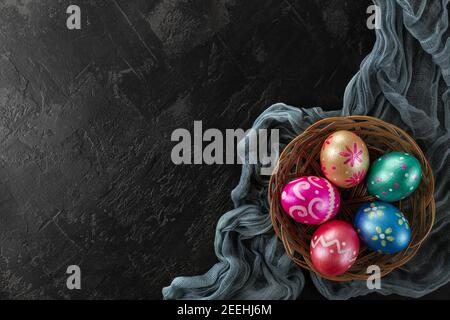 Easter eggs trendy colored deep blue, green, orange, magenta and golden decorated in basket on black background. Copy space for text. Stock Photo