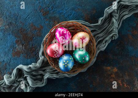Five easter eggs trendy colored deep blue, green, orange, magenta and golden decorated in basket on grunge blue background. Copy space for text. Stock Photo